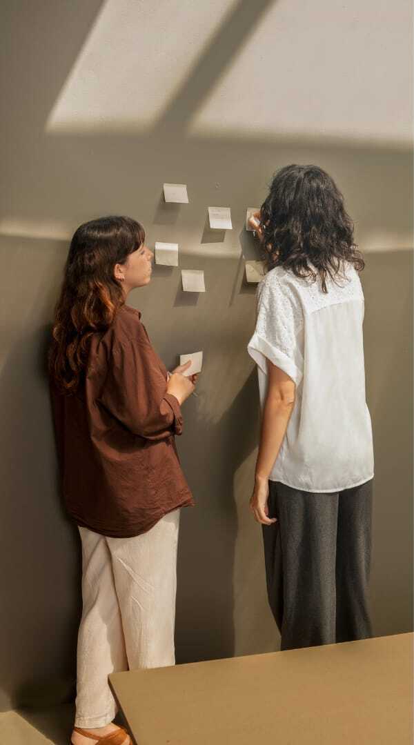 Due donne davanti a una parete tappezzata di note adesive durante una sessione di brainstorming